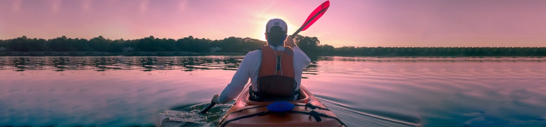 homem com kayak em rio com o pôr do sol